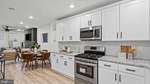 a kitchen with stainless steel appliances granite countertop a stove top oven a sink a dining table and chairs with white cabinets