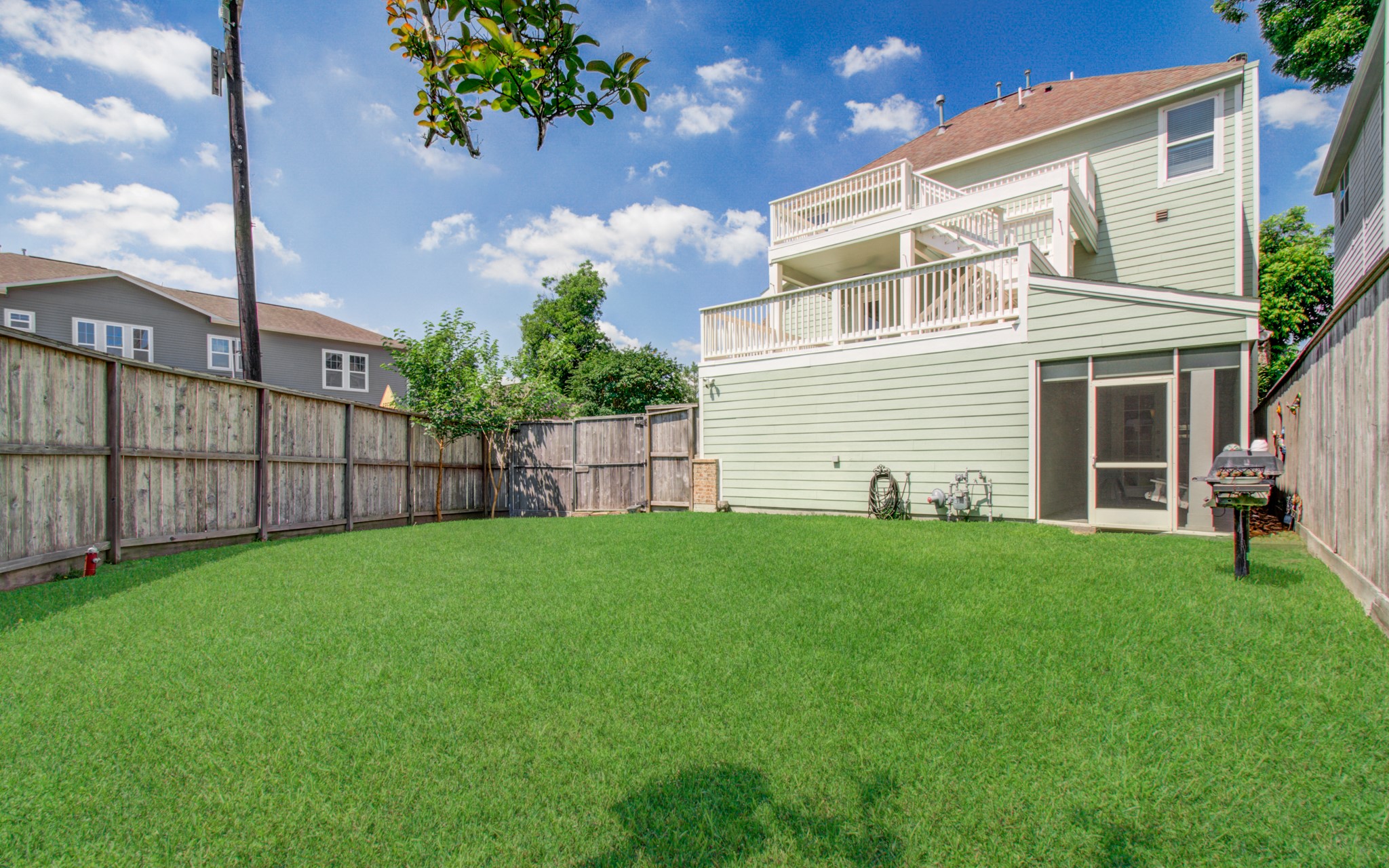 6621 North Main Street Houston, TX 77009 - Photo 33 of 41 This photo showcases a spacious, fenced backyard with lush green grass, featuring a multi-level house with large balconies and a screened-in porch, perfect for outdoor activities and relaxation.