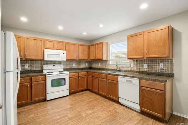 a kitchen with stainless steel appliances granite countertop a stove a sink dishwasher a refrigerator and white cabinets with wooden floor