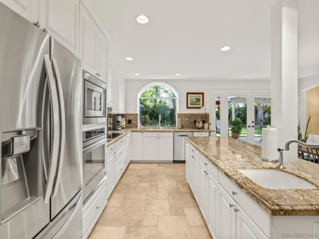 a kitchen with stainless steel appliances granite countertop a dining table chairs and white cabinets