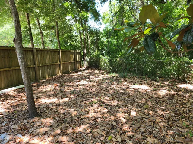 a backyard of a house with large trees and wooden fence