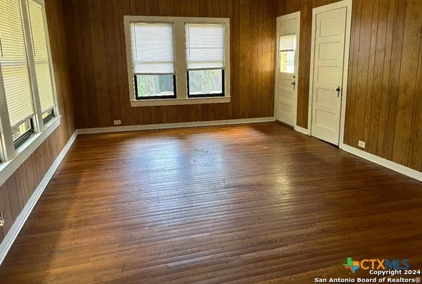 an empty room with wooden floor and windows with curtains