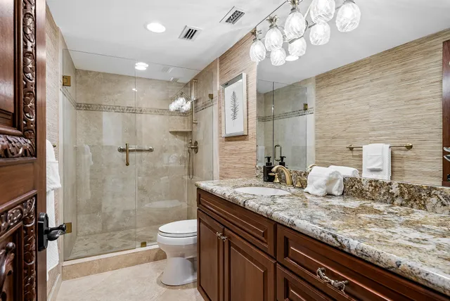 a bathroom with a granite countertop sink a toilet a mirror and shower