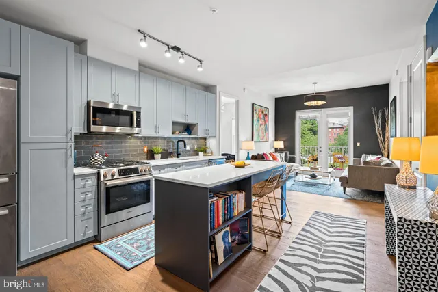 a living room with stainless steel appliances a table chairs and a book shelf