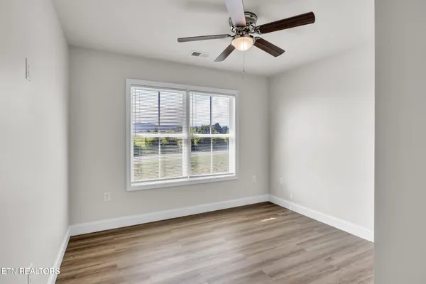 an empty room with wooden floor fan and windows