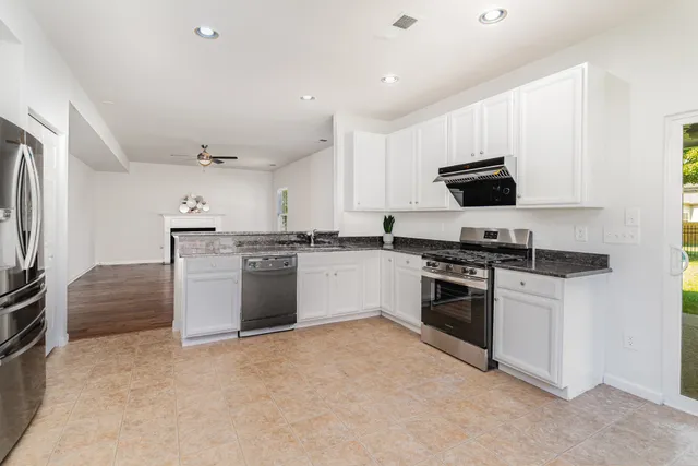 a kitchen with stainless steel appliances granite countertop a stove top oven a sink a refrigerator and white cabinets