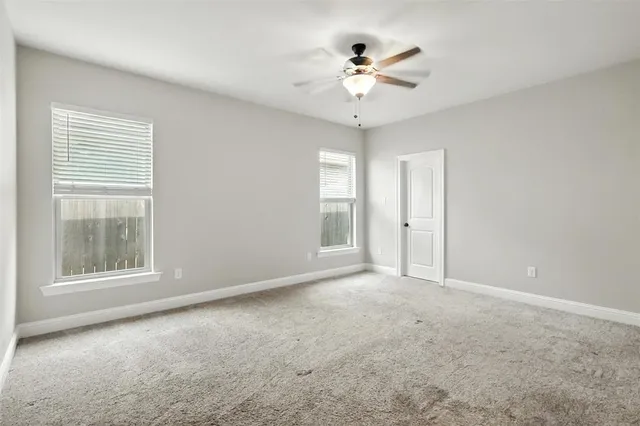 an empty room with chandelier fan and windows