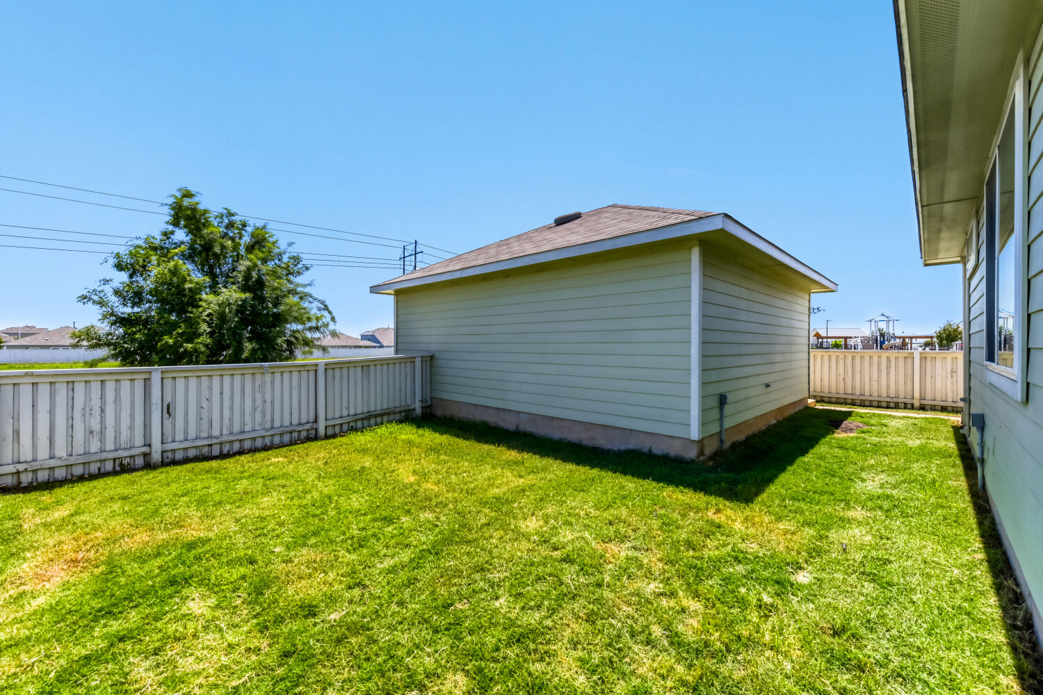 1310 Goforth Road Kyle, TX 78640 - Photo 21 of 24 Spacious side yard featuring green lawn, white picket fencing, and a detached structure with horizontal siding and a shingle roof