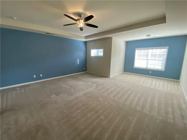 an empty room with chandelier fan and windows