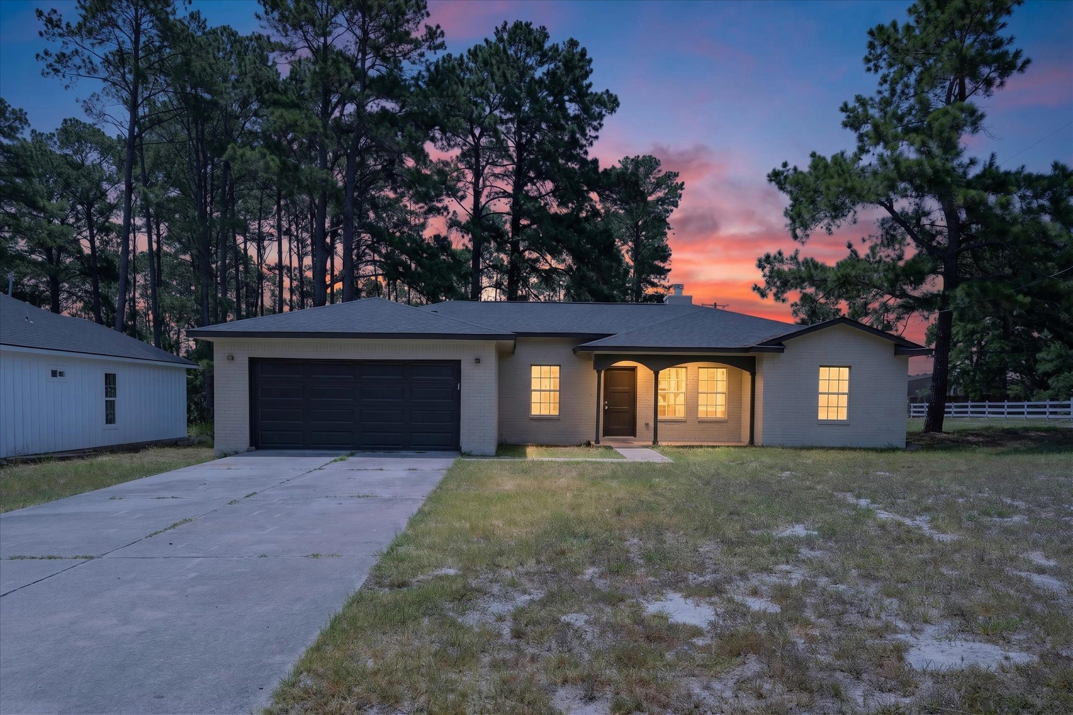 A welcoming front porch invites you into this charming home, set against a backdrop of mature trees and a vibrant twilight sky.