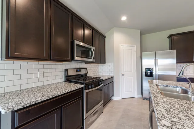 a kitchen with granite countertop stainless steel appliances a sink stove refrigerator and cabinets