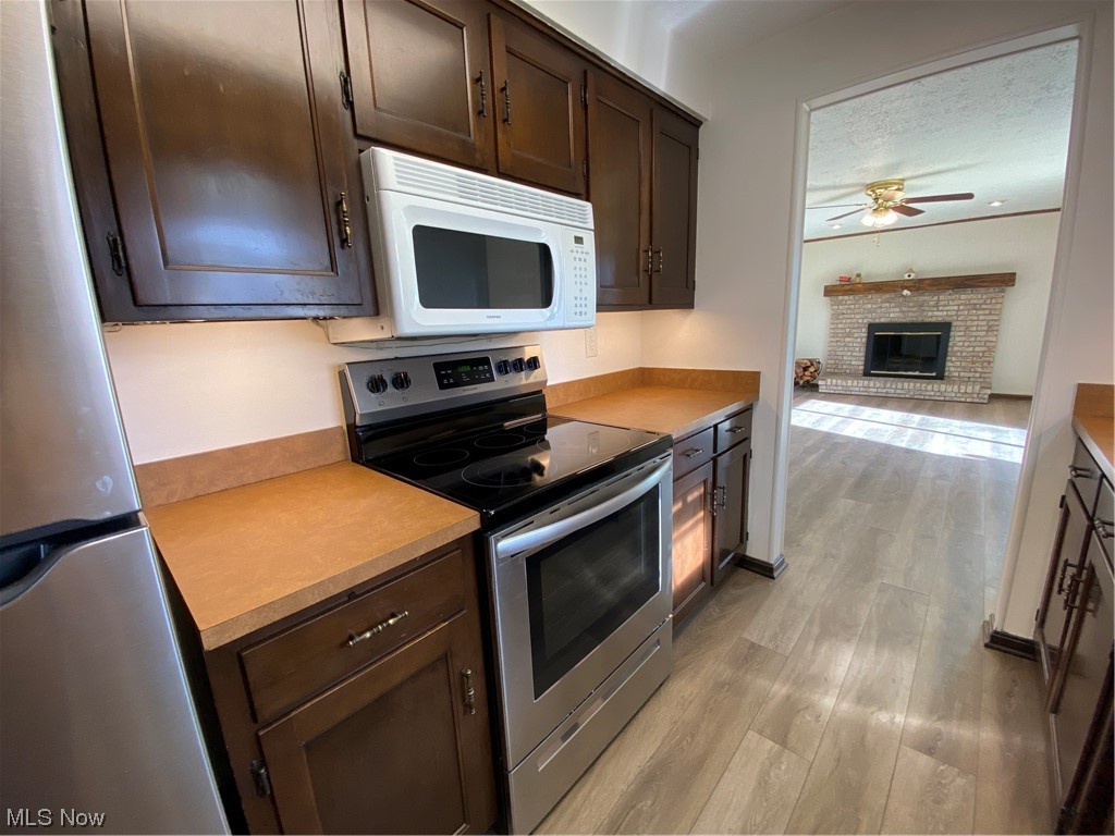 23551 Sandy Creek Road Minerva, OH 44657 - Photo 7 of 35 Kitchen with light hardwood / wood-style flooring, range, ceiling fan, a fireplace, and dark brown cabinetry
