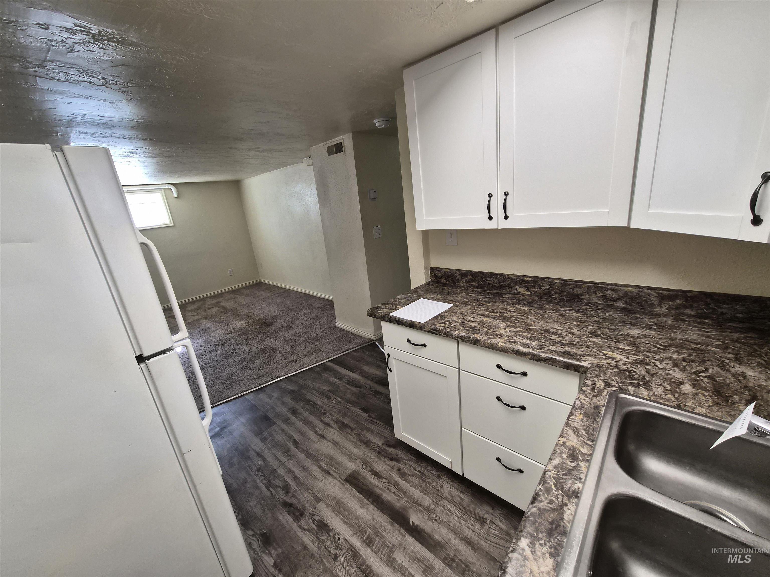 682 Randolph Avenue Pocatello, ID 83201 - Photo 29 of 29 Kitchen featuring freestanding refrigerator, white cabinetry, open floor plan, dark wood finished floors, and dark stone countertops