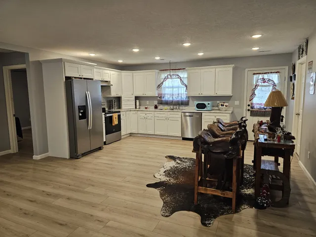 a kitchen with stainless steel appliances kitchen island granite countertop a refrigerator oven a sink a dining table and chairs with wooden floor