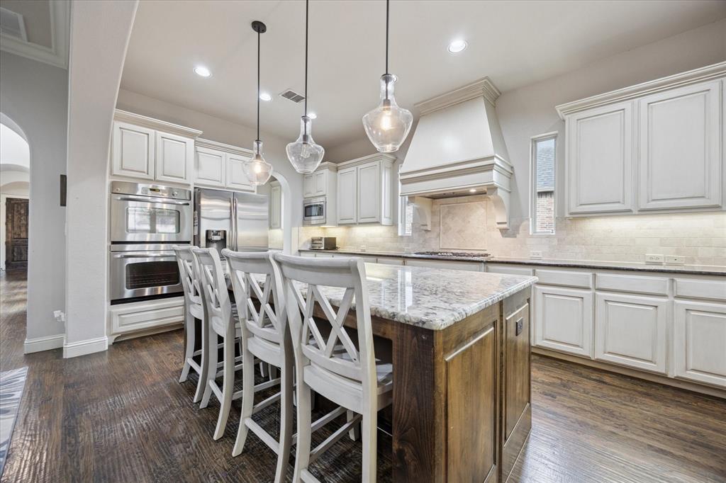 580 Butchart Drive Prosper, TX 75078 - Photo 5 of 40 Kitchen featuring arched walkways, appliances with stainless steel finishes, a kitchen island, custom range hood, and tasteful backsplash