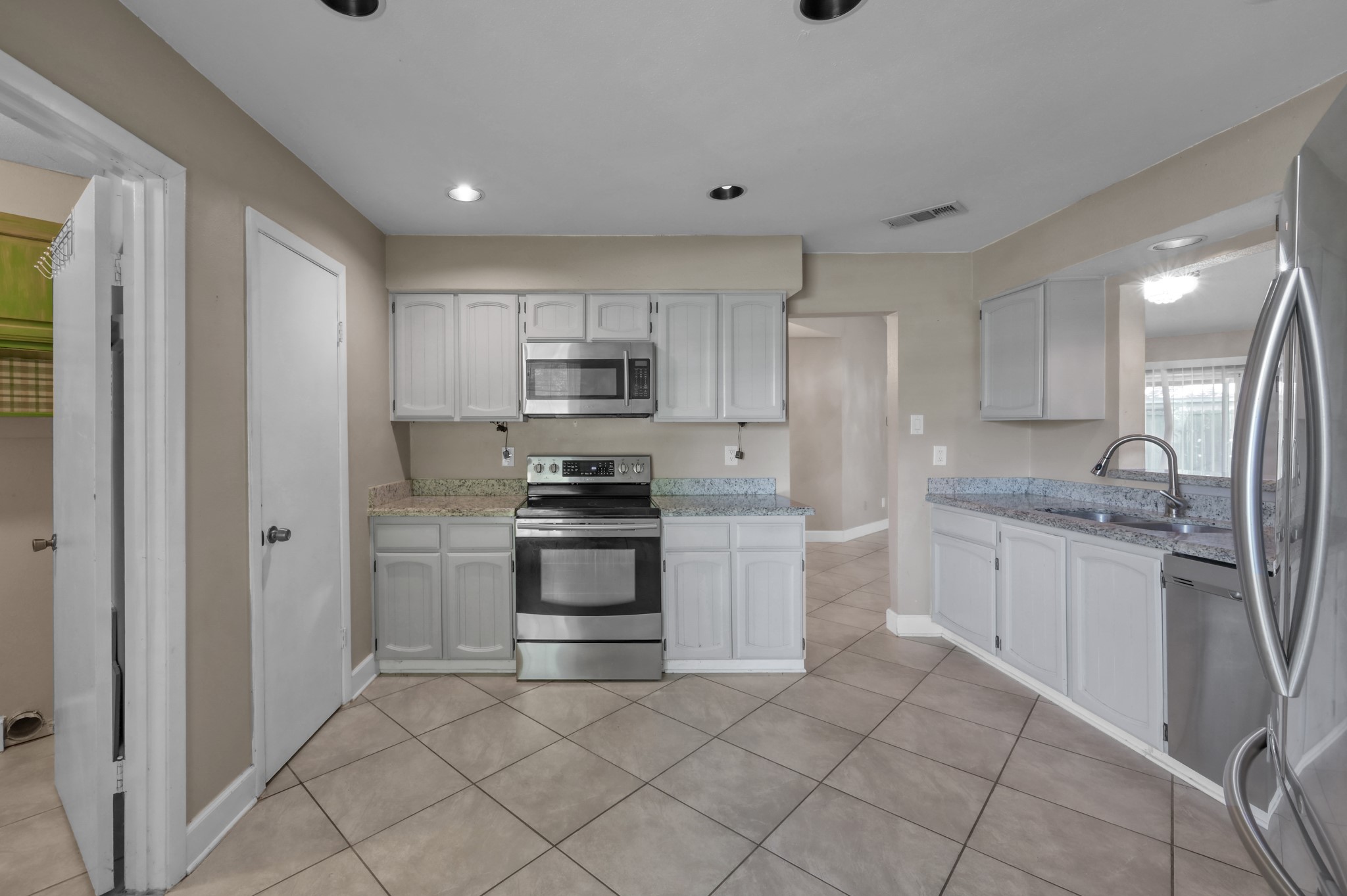12015 Fallbrook Drive Houston, TX 77065 - Photo 13 of 29 This photo showcases a modern kitchen with stainless steel appliances, white cabinetry, and granite countertops. The space features tile flooring and ample lighting, creating a bright and inviting atmosphere.