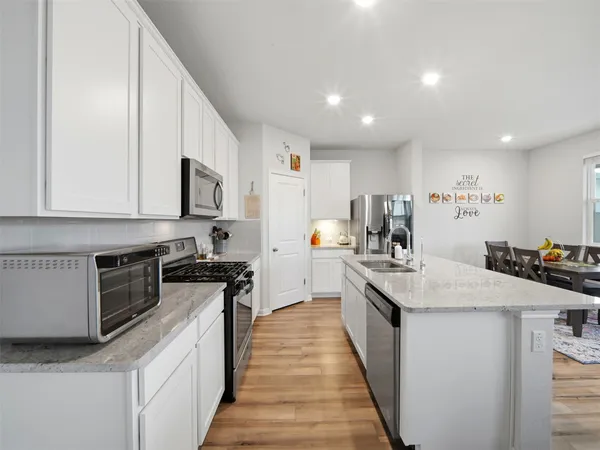 a large kitchen with stainless steel appliances granite countertop a stove top oven a sink a refrigerator and white cabinets with wooden floor