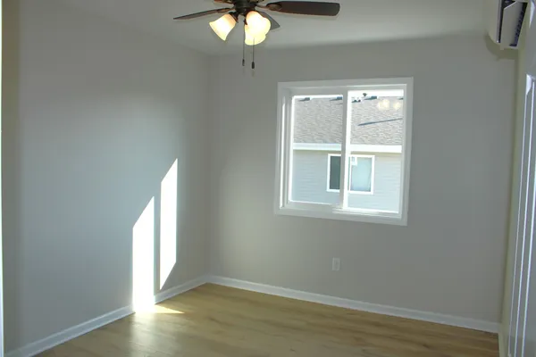an empty room with wooden floor fan and windows