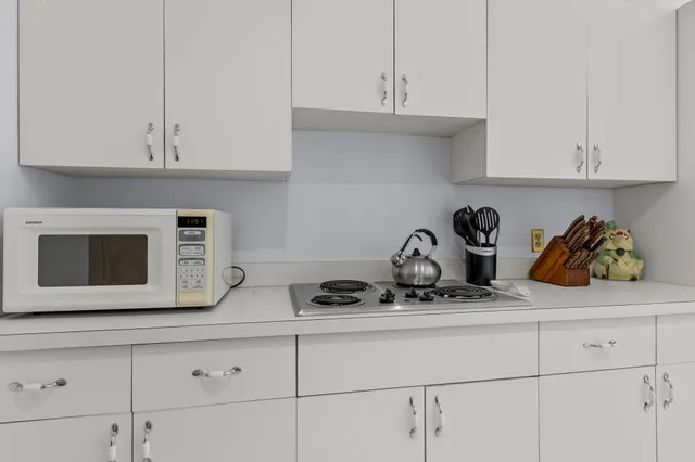 a bedroom with a bed and a lamp on dresser with wooden floor