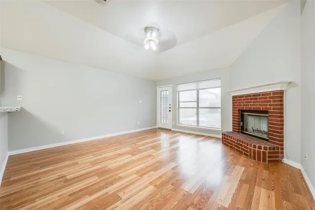 a view of an empty room with wooden floor fireplace and a window