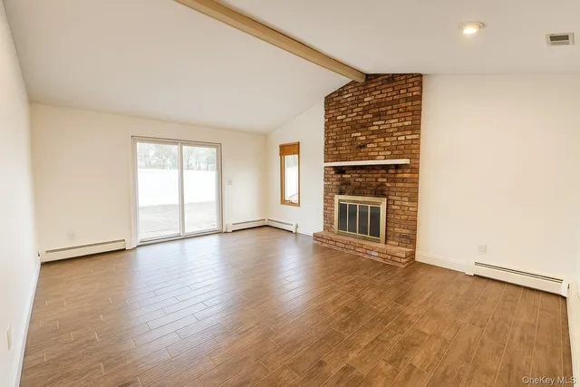 an empty room with wooden floor fireplace and windows