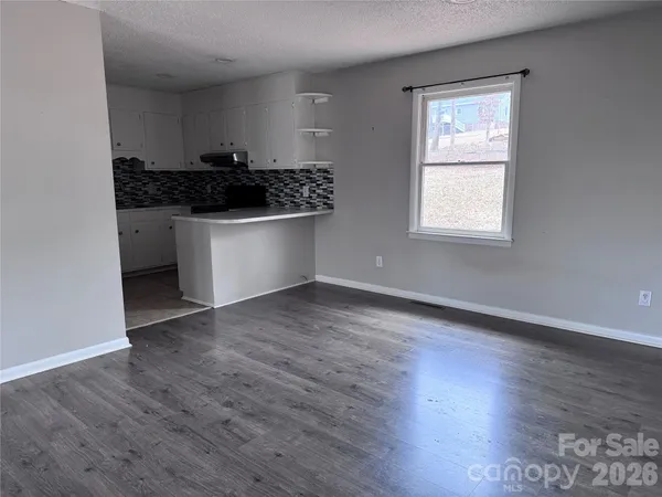 an empty room with wooden floor and kitchen view