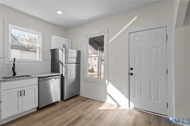 a kitchen with stainless steel appliances granite countertop a refrigerator a sink and white cabinets with wooden floor