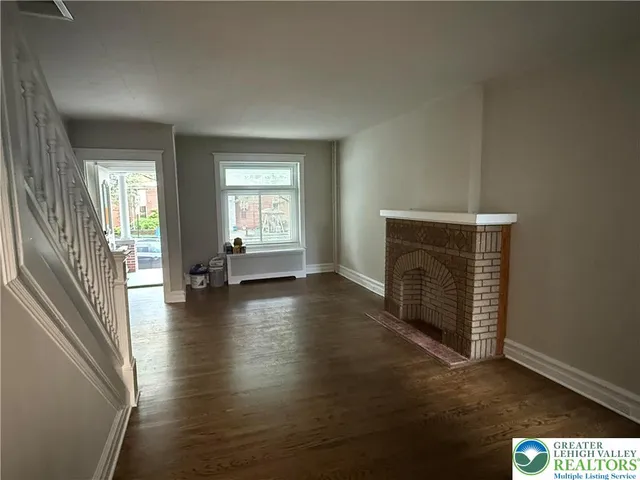 an empty room with wooden floor fireplace and windows