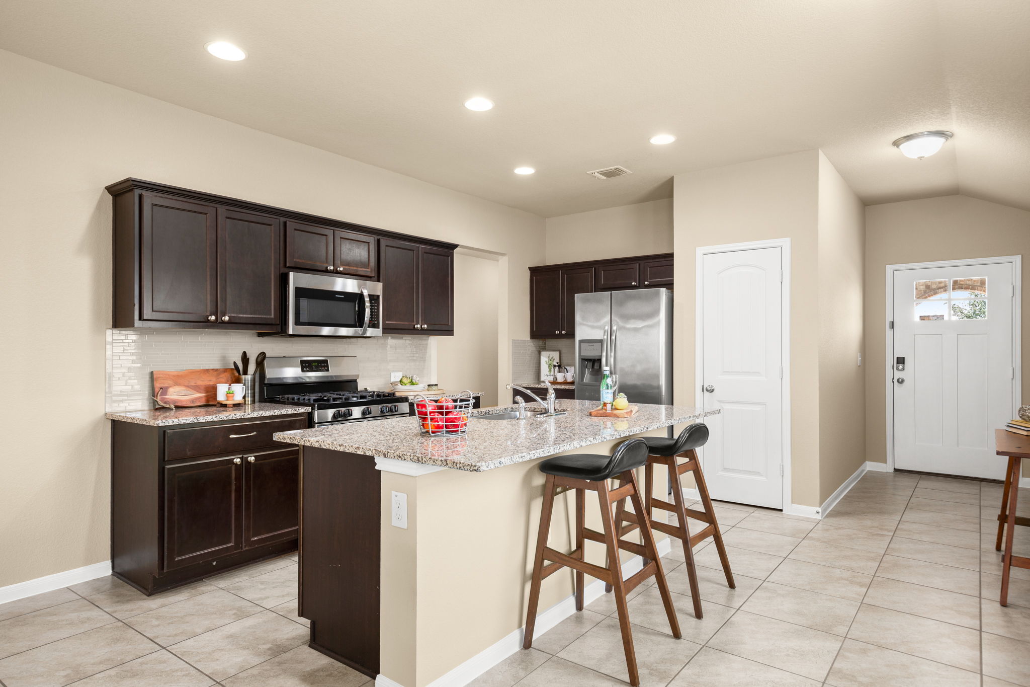 3100 Crystal Bend Drive Pflugerville, TX 78660 - Photo 11 of 32 Kitchen featuring a kitchen bar, dark brown cabinets, stainless steel appliances, light tile patterned flooring, and light stone countertops