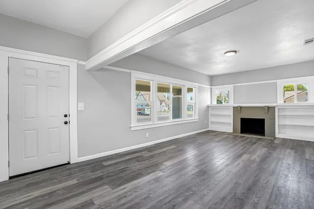 a view of an empty room with wooden floor and a window