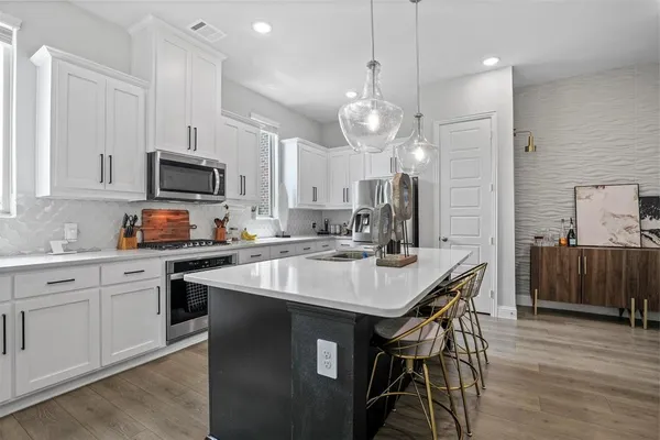 a kitchen with stainless steel appliances granite countertop a sink a stove a kitchen island a dining table and chairs with wooden floor