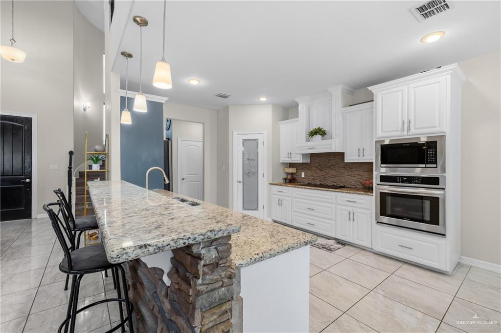 1904 Ridgeway Circle Edinburg, TX 78542 - Photo 6 of 32 Gourmet kitchen featuring a large stone-accented island with a built-in sink, pendant lighting, white cabinetry, a tile backsplash, and stainless steel built-in appliances