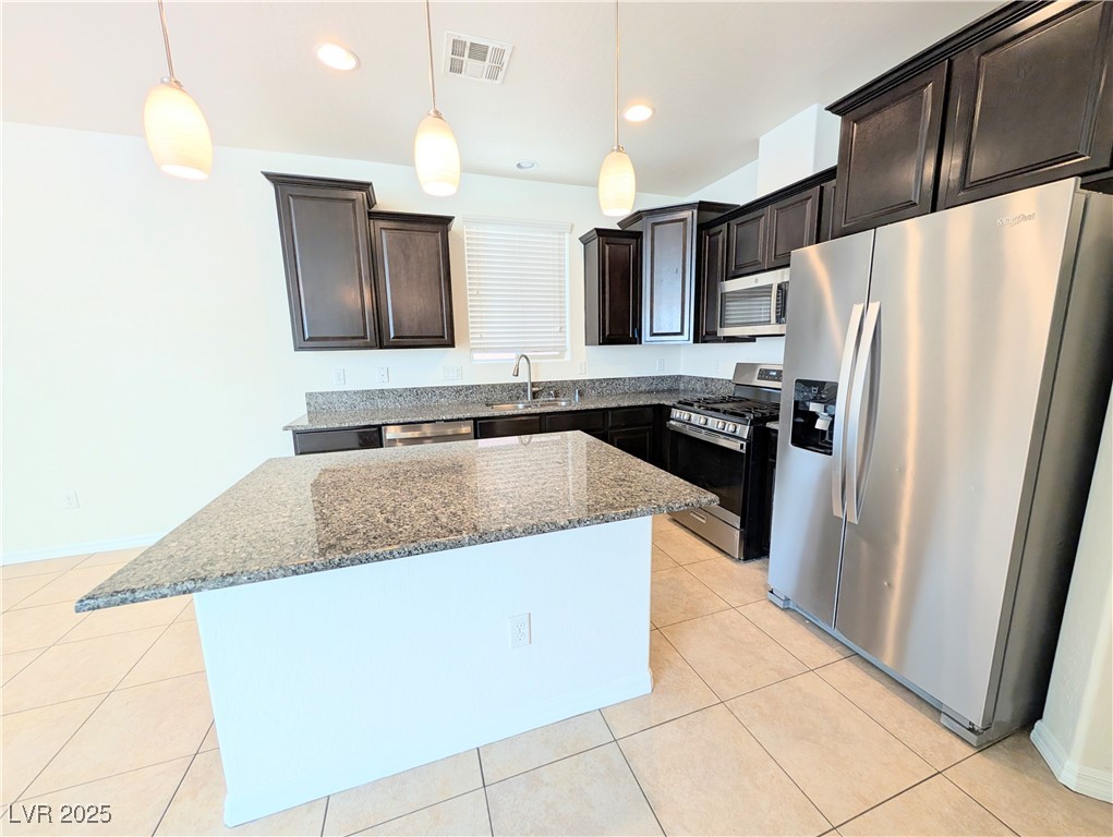 7011 Amapa Road Las Vegas, NV 89178 - Photo 4 of 32 Kitchen featuring appliances with stainless steel finishes, dark stone countertops, light tile patterned floors, hanging light fixtures, and a center island