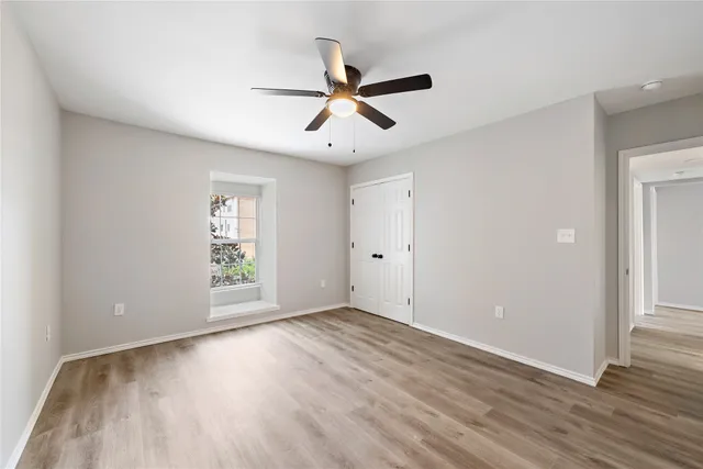 an empty room with wooden floor fan and windows