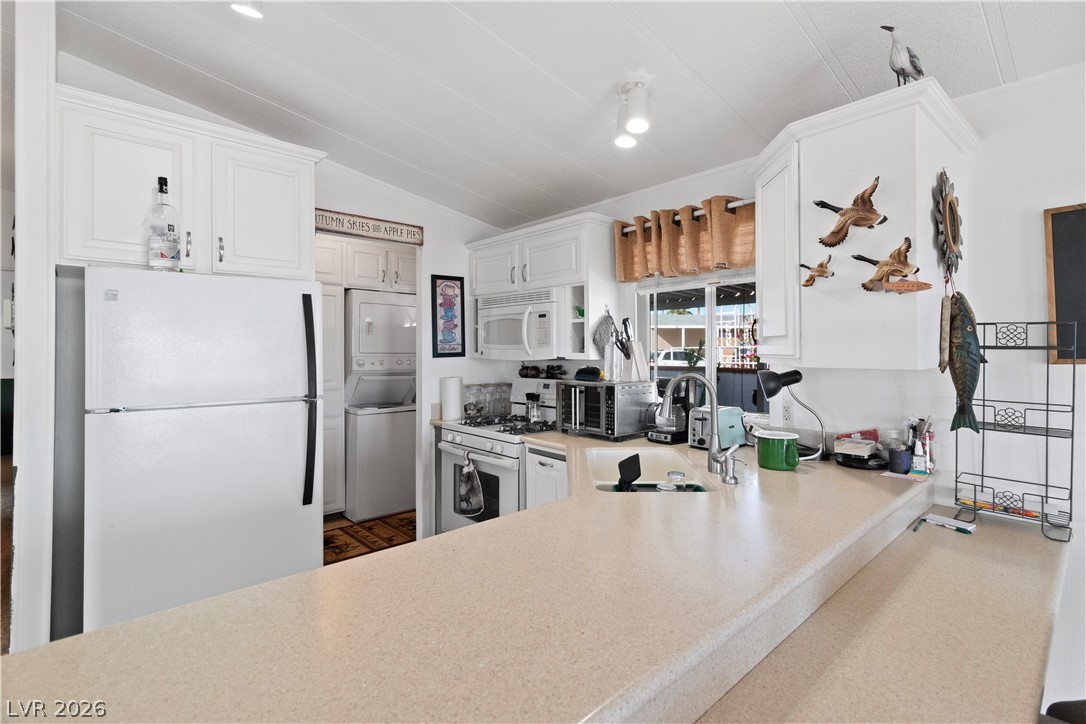 1655 Granada Street Laughlin, NV 89029 - Photo 13 of 76 Kitchen with white appliances, light countertops, white cabinetry, vaulted ceiling, and stacked washer and dryer