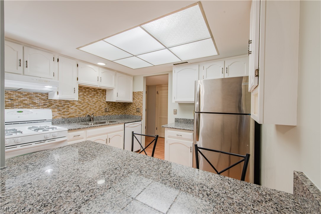 22701 Center Ridge Road, Unit 207 Rocky River, OH 44116 - Photo 11 of 26 Kitchen featuring white appliances, light stone countertops, white cabinetry, and tasteful backsplash