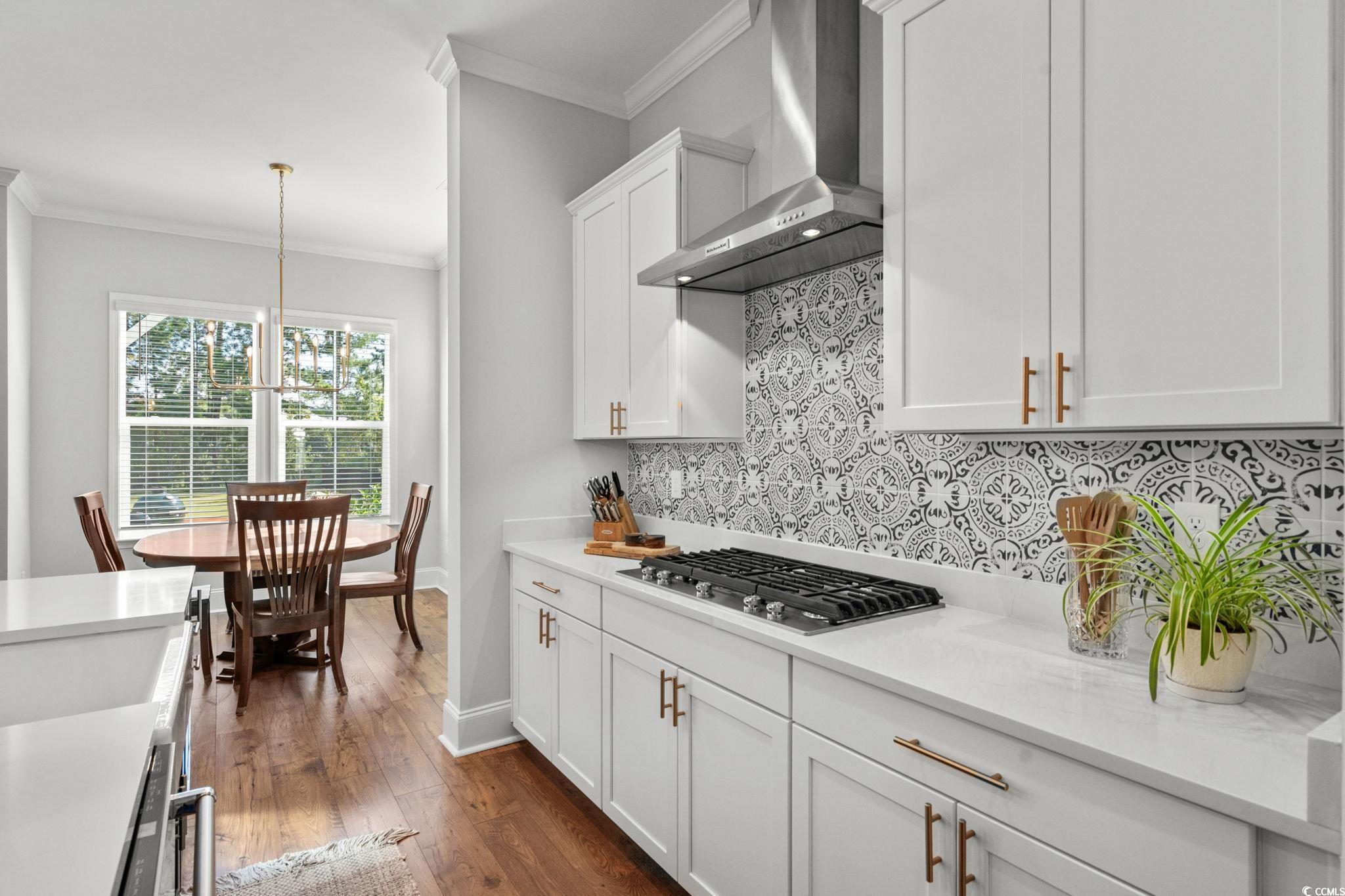 191 Blackwater Drive Murrells Inlet, SC 29576 - Photo 11 of 40 Kitchen featuring decorative backsplash, crown molding, wall chimney range hood, white cabinetry, and pendant lighting