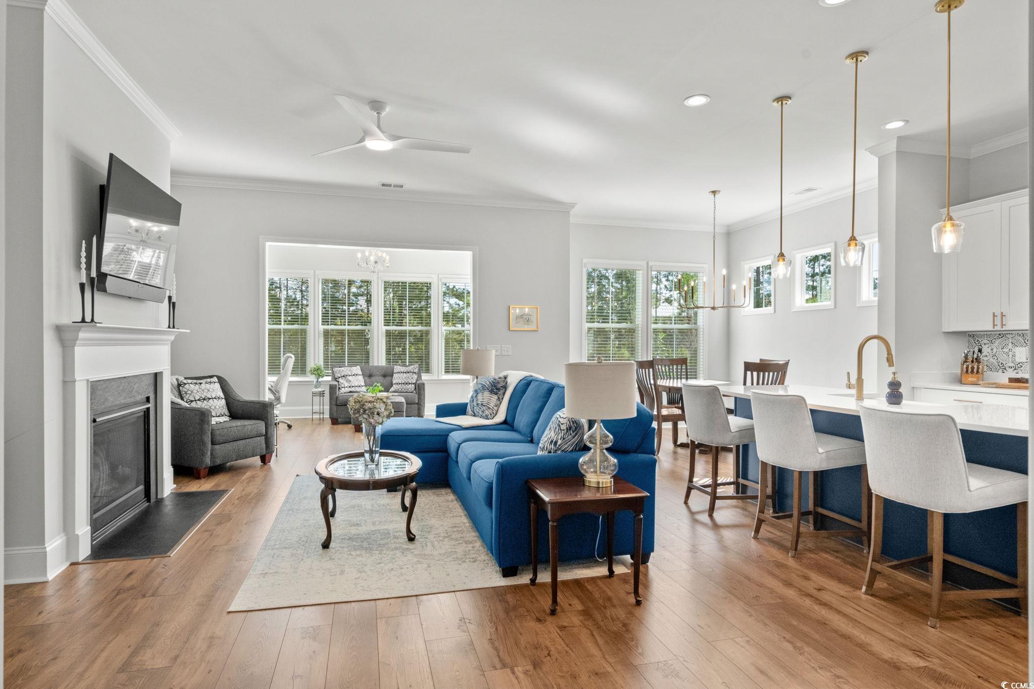 191 Blackwater Drive Murrells Inlet, SC 29576 - Photo 5 of 40 Living area featuring crown molding, light wood-style flooring, a glass covered fireplace, ceiling fan, and a chandelier