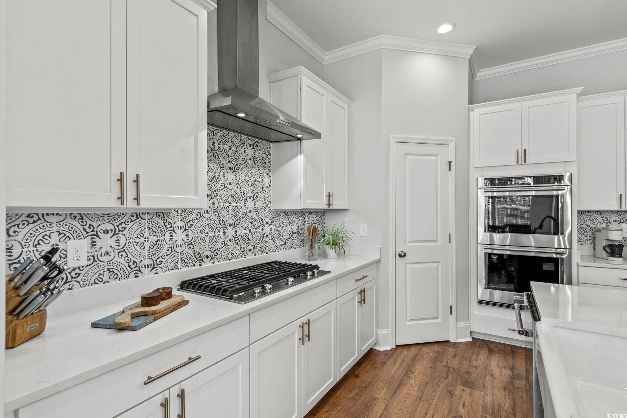 191 Blackwater Drive Murrells Inlet, SC 29576 - Photo 10 of 40 Kitchen with decorative backsplash, white cabinetry, wall chimney exhaust hood, crown molding, and appliances with stainless steel finishes