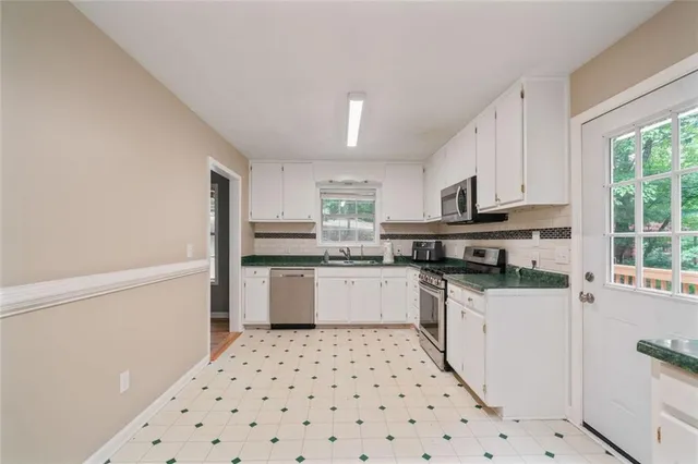 a kitchen with granite countertop a refrigerator oven a sink a stove and white cabinets