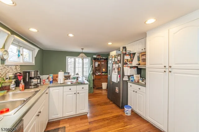 a kitchen with stainless steel appliances kitchen island granite countertop a refrigerator a sink dishwasher and white cabinets with wooden floor