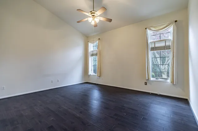 an empty room with wooden floor chandelier fan and windows