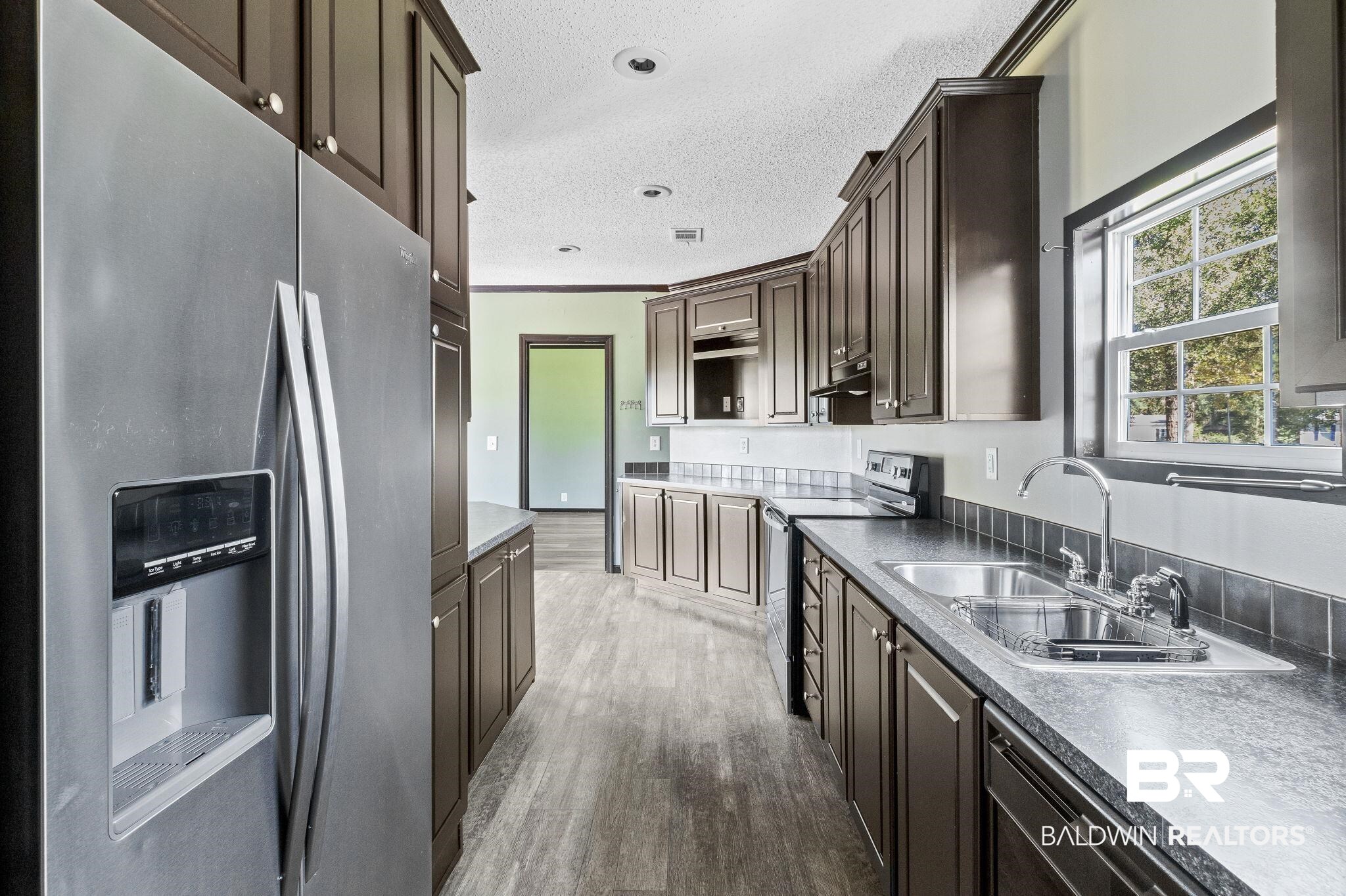 6870 Cecilia Court Theodore, AL 36582 - Photo 23 of 83 Kitchen with appliances with stainless steel finishes, dark brown cabinets, hardwood / wood-style floors, and a textured ceiling