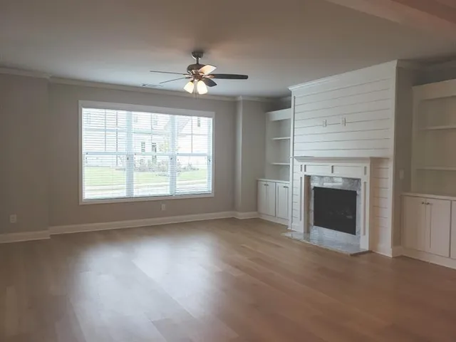 a view of an empty room with wooden floor fireplace and a window