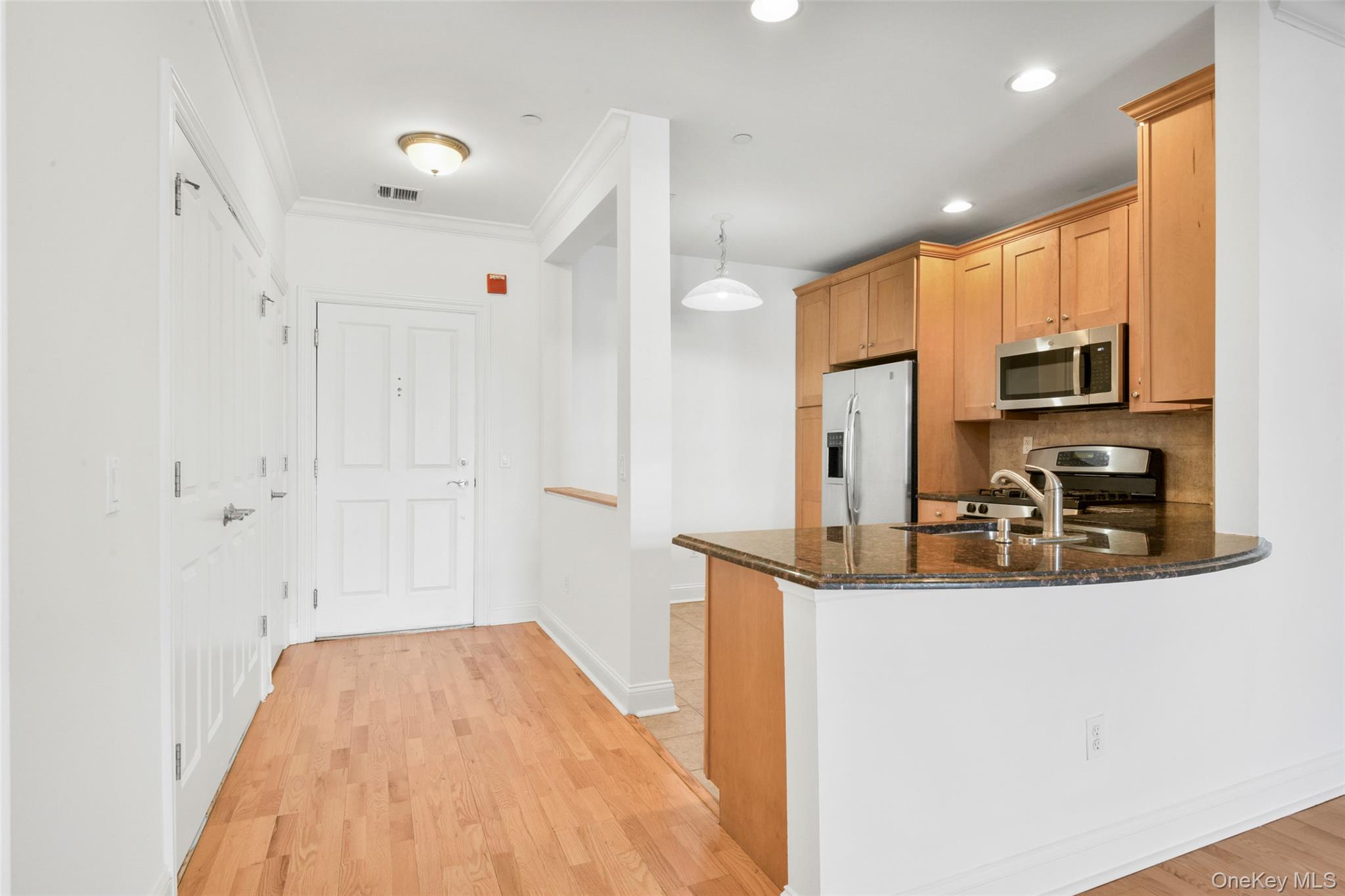 55 1st Street, Unit 207 Pelham, NY 10803 - Photo 4 of 23 Kitchen with dark stone countertops, stainless steel appliances, decorative light fixtures, ornamental molding, and light wood-style floors