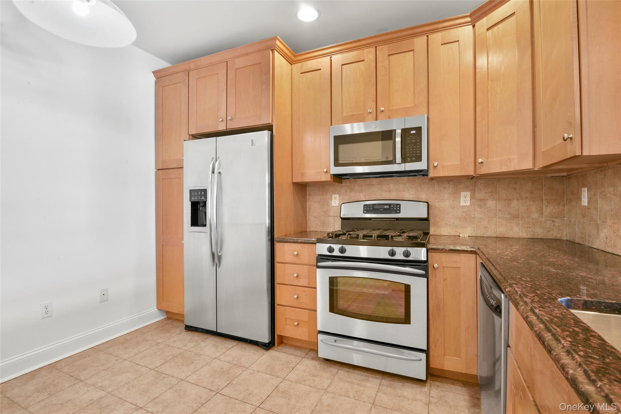 55 1st Street, Unit 207 Pelham, NY 10803 - Photo 5 of 23 Kitchen featuring appliances with stainless steel finishes, dark stone countertops, backsplash, light brown cabinets, and light tile patterned floors