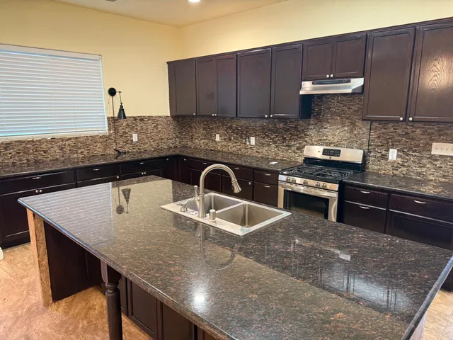 a kitchen with granite countertop a sink a stove and cabinets