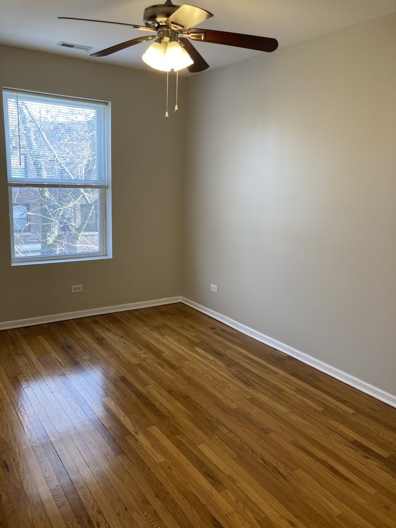 4042 South Calumet Avenue, Unit 3S Chicago, IL 60653 - Photo 9 of 11 an empty room with wooden floor chandelier fan and windows