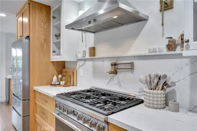 a large white kitchen with stainless steel appliances granite countertop a stove a sink a refrigerator and white cabinets