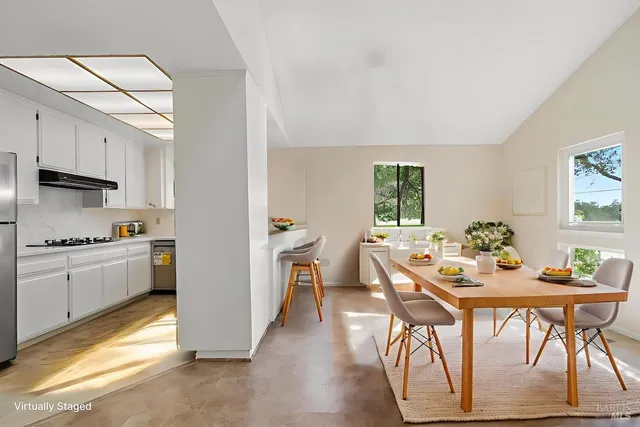 a kitchen with stainless steel appliances kitchen island granite countertop a dining table chairs and a refrigerator